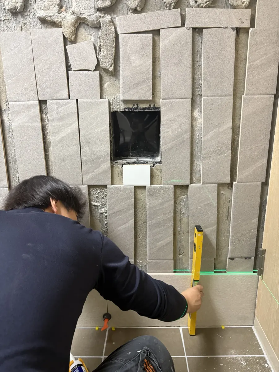 욕조 벽타일 교체 관련 서비스, 화장실 벽타일 교체 안내 — 세로로 자른 타일 조각을 벽에 붙이며 수평을 확인하는 모습